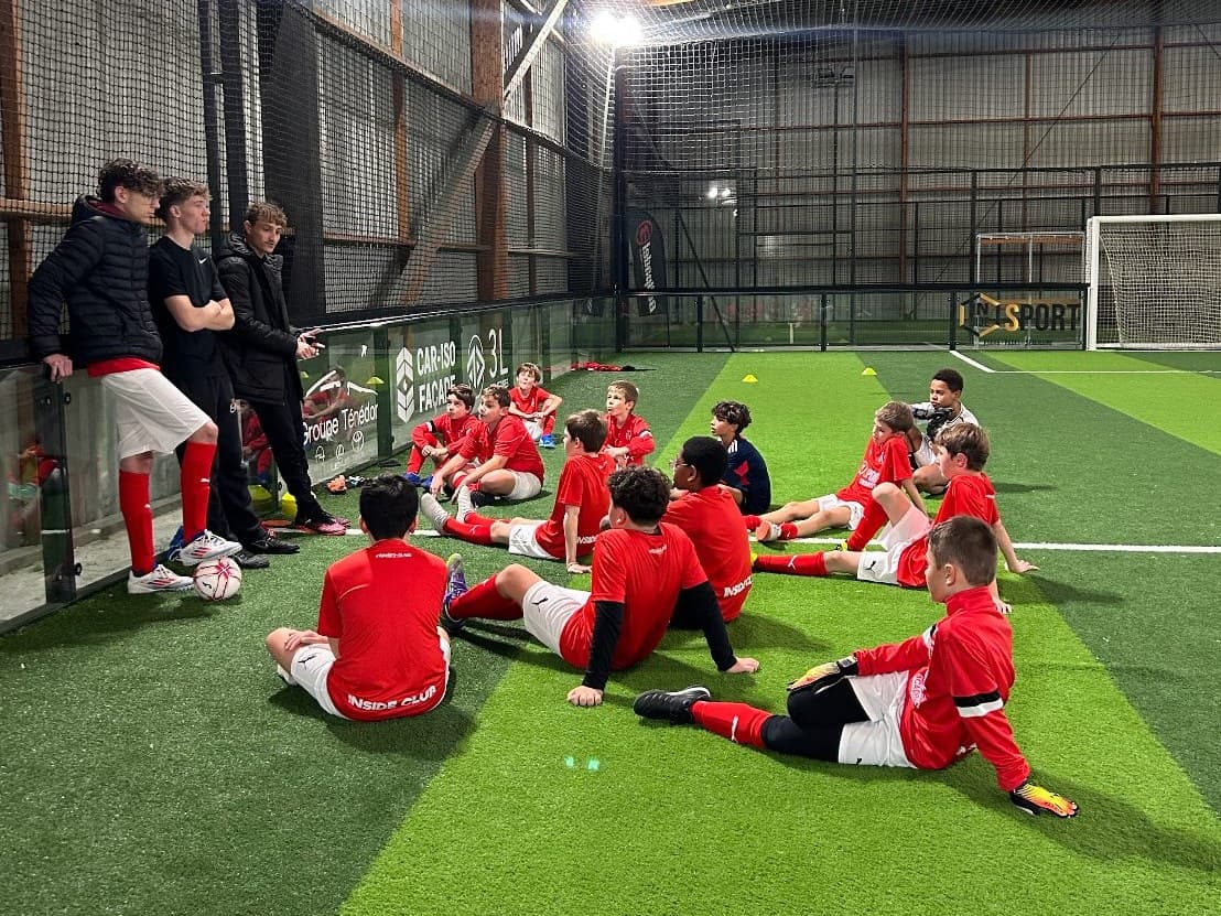 Inside Academy children sitting on the pitch during a session